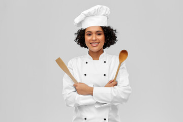 cooking, culinary and people concept - happy smiling female chef in toque with wooden spoon and...