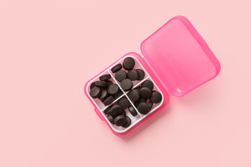 Container with activated carbon pills on pink background