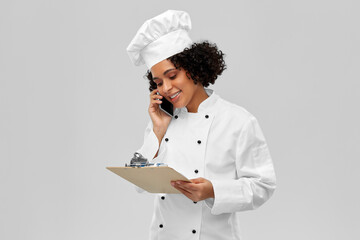 cooking, culinary and people concept - happy smiling female chef in toque with clipboard calling on smartphone over grey background