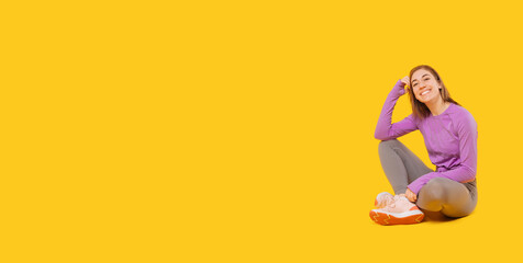 Young woman in sportswear is smiling and sitting down on yellow background.