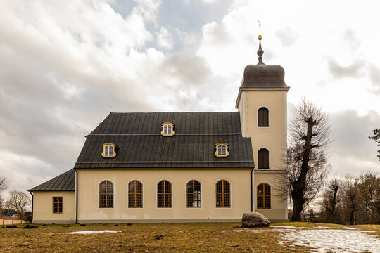 Low angle sideways photo to St. Catherine's Lutheran Church in Riga, Latvia at early spring. Light yellow Lutheran church at grey cloudy winter. Parish church with pruned trees.