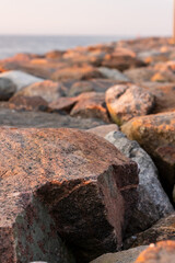 Rocks on the beach at sunset. Sun is setting over the breakwater at calm evening. Rock pier at sea coast during pink sundown. Sea rocks during dusk.
