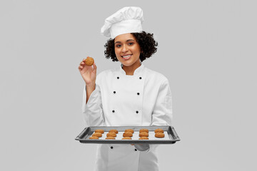 cooking, culinary and bakery concept - happy smiling female chef or baker in white toque and jacket holding baking tray with oatmeal cookies over grey background - obrazy, fototapety, plakaty