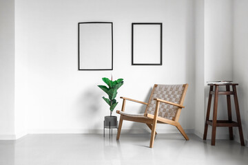 Comfortable armchair, houseplant and blank photo frames on wall in light room interior