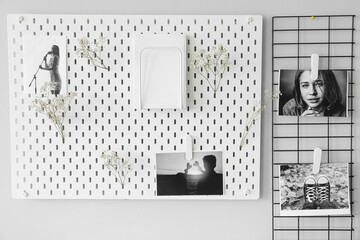 Stylish peg board with photos and book hanging on light grey wall