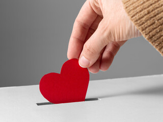 charity, love and valentine's day concept - close up of hand putting red heart into donation box