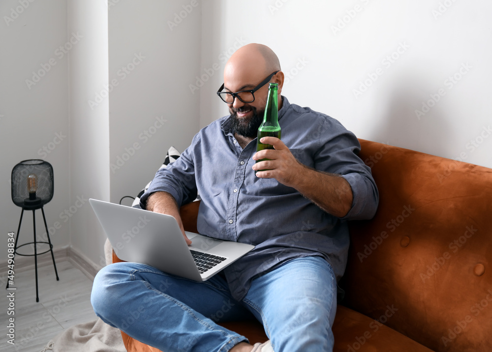 Wall mural Man with laptop drinking beer at home