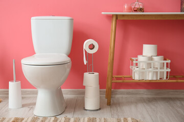 Naklejka na ściany i meble Holder with rolls of paper, toilet bowl and table near pink wall