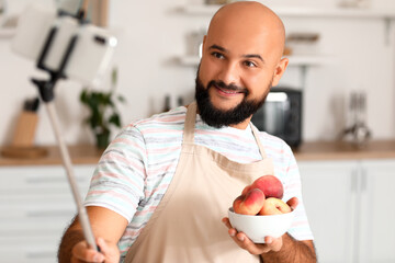 Handsome man with bowl of peaches recording video tutorial in kitchen