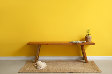 Obraz premium Wooden bench with magazines, flowerpot and slippers near yellow wall