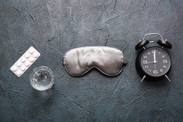 Sleep mask, alarm clock, glass of water and pills on grey background