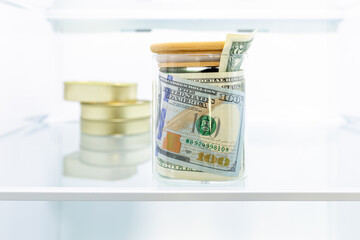 Money, cash banknotes, US dollars in a glass jar and canned food in the refrigerator. Cash saving...