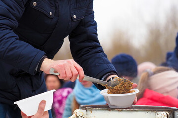 Volunteers feed refugees porridge from the field kitchen on street. Share with the needy