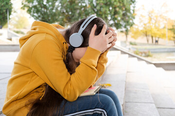 Sad teenage girl in headphones will cover her face with her hands, a place for text