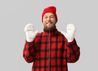 Young bearded man in warm gloves and hat on light background