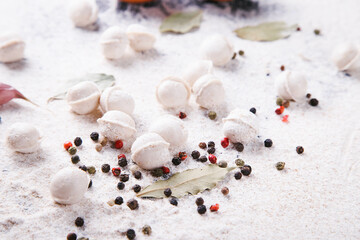 Raw dumplings on the background of flour with peppercorns and bay leaf