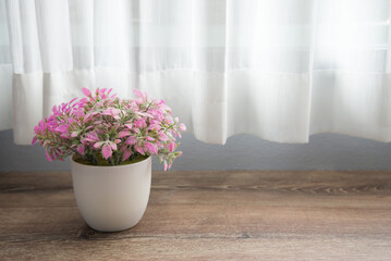 Artificial purple leaves flower plant in white cup on wooden table with curtain background and sunlight. Decoration, relax and lifestyle concept.