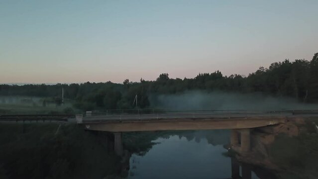 An early foggy morning in the countryside outside the city. Lonely road, bridge, church, fog, forest around, river