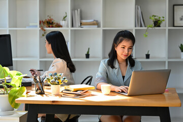 A portrait of pretty Asian businesswomen sitting in the office working on a laptop and computer, for business and technology concept.