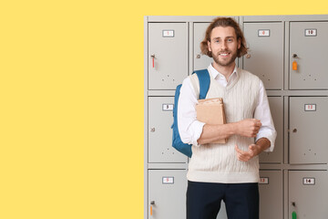 Male student with books near locker on yellow background