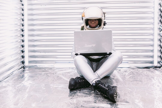 Black astronaut browsing laptop in spaceship