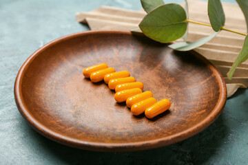 Plate with turmeric powder capsules on color background, closeup