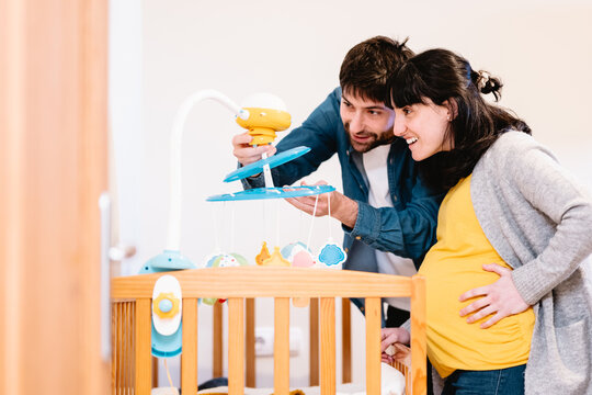 Cheerful man and pregnant woman with crib in room