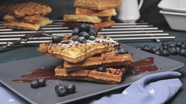weiche, zarte belgische Waffeln mit frischen Blaubeeren und Schokoladensauce, bestreut mit s&uuml;ssem Puderzucker auf grauem Teller