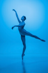 Fototapeta na wymiar Young and graceful ballet dancer isolated on blue studio background in neon light. Art, motion, action, flexibility, inspiration concept.