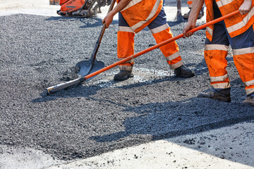 A working team of road builders manually levels the hot asphalt with shovels and metal levels.