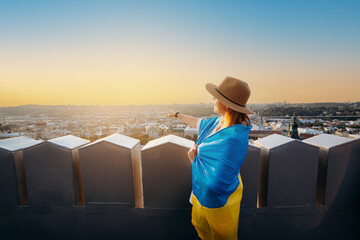 Fototapeta premium A woman stands with the national Ukrainian flag and waving it praying for peace at sunset in Lviv..A symbol of the Ukrainian people, independence and strength. Pray for Ukraine.
