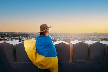 Fototapeta premium A woman stands with the national Ukrainian flag and waving it praying for peace at sunset in Lviv..A symbol of the Ukrainian people, independence and strength. Pray for Ukraine.