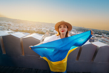Obraz premium A woman stands with the national Ukrainian flag and waving it praying for peace at sunset in Lviv..A symbol of the Ukrainian people, independence and strength. Pray for Ukraine.