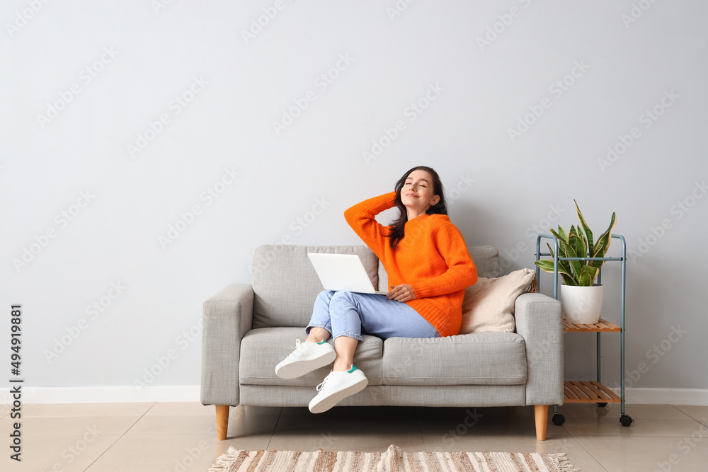 Poster Beautiful young woman with laptop resting on couch at home