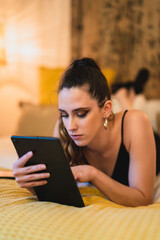 Chica joven delgada con pelo largo mirando tablet sobre la cama de un hotel estilo soho