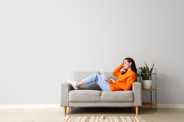 Beautiful young woman with laptop resting on couch at home - Powered by Adobe