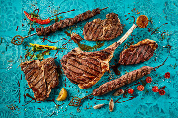 High angle shot of tasty grilled meat steaks and spicy sauces on a blue table with fresh tomatoes