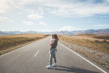 Fototapeta premium mother and daughter in full growth on a trip to the Caucasus, on a beautiful road jyly su in autumn against the backdrop of Mount Elbrus in Russia