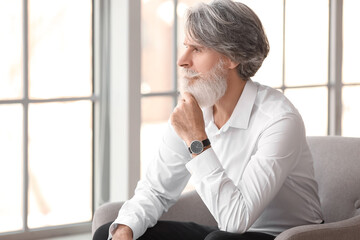 Fototapeta premium Portrait of handsome mature bearded man sitting in armchair at home