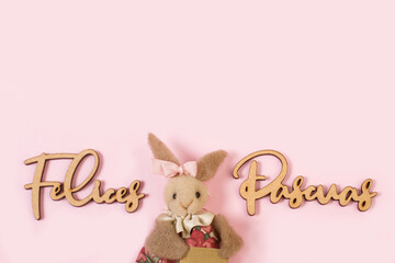 Conejita junto a la pañabra Felices Pascuas de madera sobre un fondo rosa pastel liso y aislado....