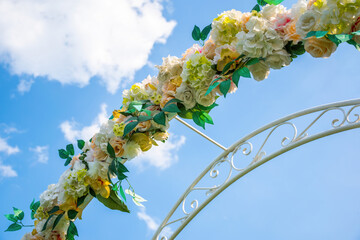 Floral arch detail. Wedding decoration outdoors. Cumulus clouds on a background of blue sky.