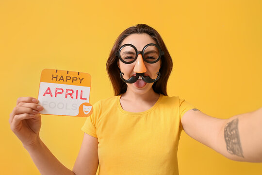 Young woman in funny disguise taking selfie on yellow background. April fools' day celebration