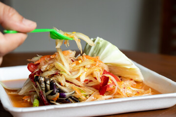 Female hand hold fork with Papaya salad, Thai food name Som Tum, on white foam plate
