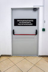 Closed emergency exit door. Text in russian: emergency exit, do not block, under alarm