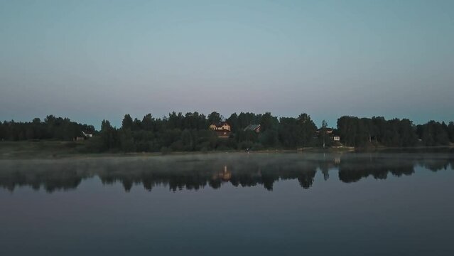 Mist over the river in the early morning dawn. A group of young people resting and singing songs on the shore, woods and countryside in the background 