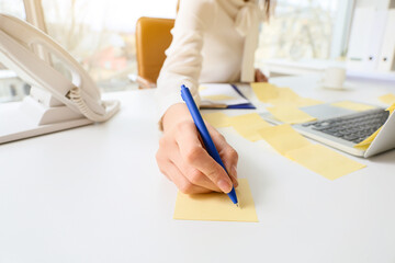 Young manager writing on sticky note paper at her workplace