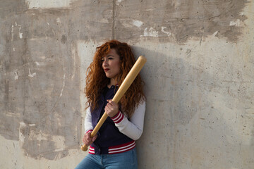 young and beautiful redhead woman is happy with jacket, baseball bat and jeans, she is posing in...