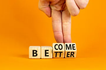 Fotobehang Become better symbol. Businessman turns wooden cubes and changes the concept word Better to Become. Beautiful orange table orange background. Business become better concept. Copy space. © Dzmitry