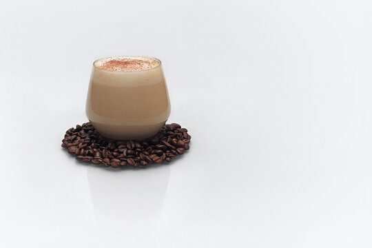 Cup of coffee sprinkled with powder on a trivet made of coffee beans on a white background