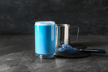 Glass of blue matcha tea and spoon with powder on dark grunge background